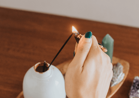 A hand lighting a piece of bakhoor incense over a white burner