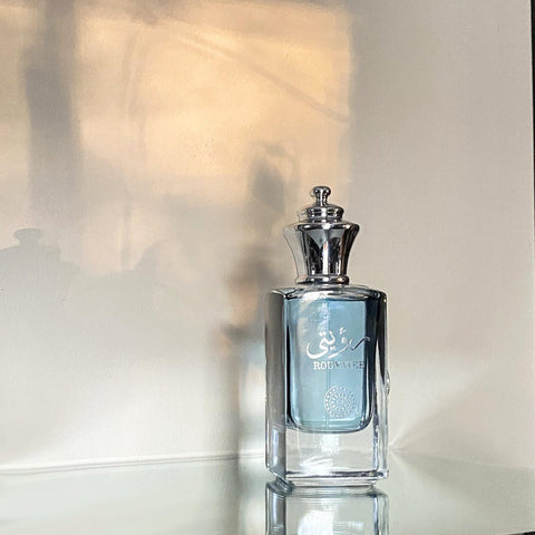 A clear glass perfume bottle with a silver cap and 'ROUYATEE' branding on a reflective surface.